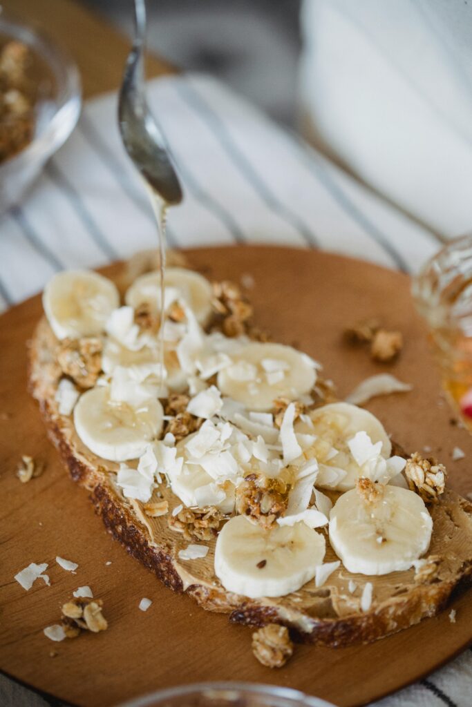 Close-up of banana and granola topped toast with syrup pouring, perfect for breakfast or brunch ideas.
